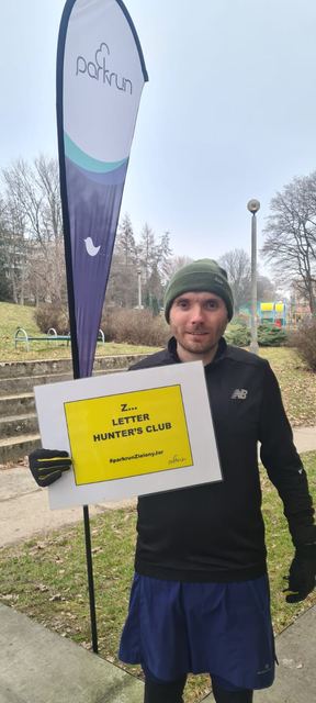 Runner holding a Parkrun sign beside a Parkrun banner